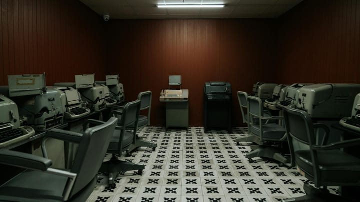 A vintage office room filled with old typewriters and chairs, evoking a 1940s-1960s era ambiance.